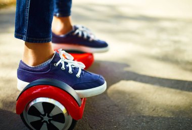 Legs of woman riding gyroboard. Person on white hoverboard. Electriic hyroscooter driving. Self-balancing two-wheeled board or hoverboard scooter. clipart