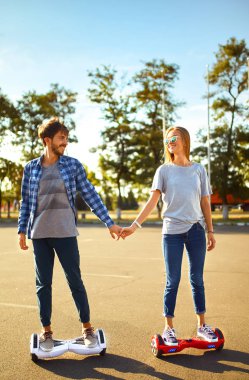 Mutlu adam ve kadın şehirde birlikte rahatlamak için Hoverboard 'a biniyorlar. Parkta uçan kaykaya binen genç bir çift, dengeli scooter kullanıyorlar. Aktif yaşam tarzı teknolojisi gelecek.