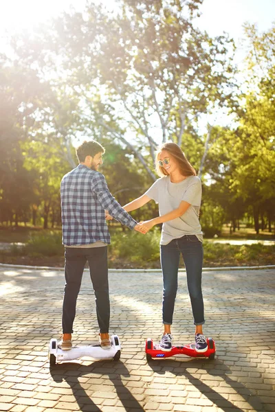 Happy man and woman riding on the Hoverboard for relaxing time together outdoor at the city. A young couple riding a hoverboard in a park, self-balancing scooter. Active lifestyle technology future.