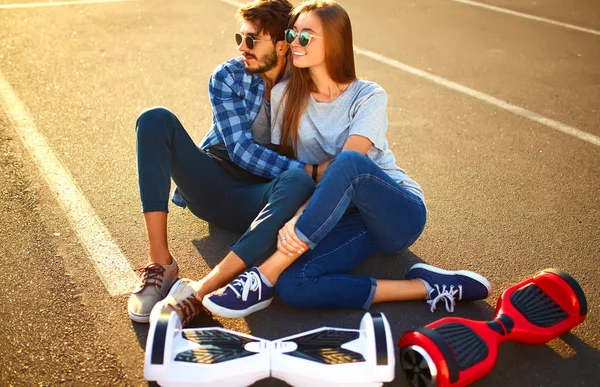 市内の屋外で一緒にリラックスした時間を過ごすためにホバーボードに乗って幸せな男と女 公園でホバーボードに乗っている若いカップル 自己バランススクーター アクティブライフスタイルテクノロジーの未来 — ストック写真