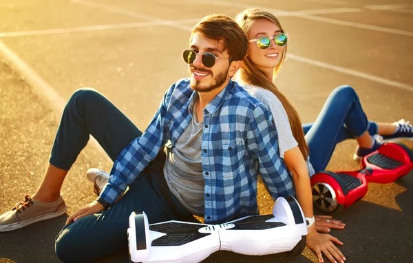 市内の屋外で一緒にリラックスした時間を過ごすためにホバーボードに乗って幸せな男と女 公園でホバーボードに乗っている若いカップル 自己バランススクーター アクティブライフスタイルテクノロジーの未来 — ストック写真