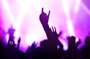 Bir müzik festivalinde seyirciler ellerini kaldırdı ve sahnenin üstünden ışıklar süzülüyor. Kalabalık ellerini kaldırıyor, dans ediyor ve konserin tadını çıkarıyor..