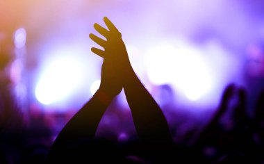 Bir müzik festivalinde seyirciler ellerini kaldırdı ve sahnenin üstünden ışıklar süzülüyor. Kalabalık ellerini kaldırıyor, dans ediyor ve konserin tadını çıkarıyor..