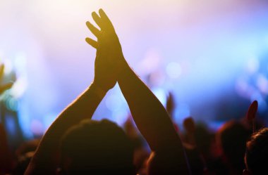 Bir müzik festivalinde seyirciler ellerini kaldırdı ve sahnenin üstünden ışıklar süzülüyor. Kalabalık ellerini kaldırıyor, dans ediyor ve konserin tadını çıkarıyor..