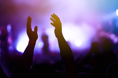 Bir müzik festivalinde seyirciler ellerini kaldırdı ve sahnenin üstünden ışıklar süzülüyor. Kalabalık ellerini kaldırıyor, dans ediyor ve konserin tadını çıkarıyor..
