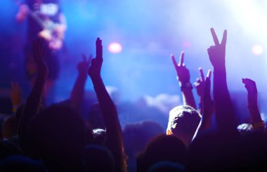 Bir müzik festivalinde seyirciler ellerini kaldırdı ve sahnenin üstünden ışıklar süzülüyor. Kalabalık ellerini kaldırıyor, dans ediyor ve konserin tadını çıkarıyor..