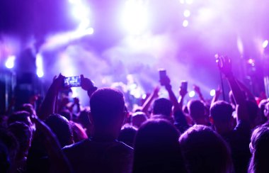 Bir müzik festivalinde seyirciler ellerini kaldırdı ve sahnenin üstünden ışıklar süzülüyor. Kalabalık ellerini kaldırıyor, dans ediyor ve konserin tadını çıkarıyor..