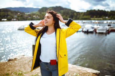 Genç kadın Norveç 'teki dağların arka planında özgürlüğün tadını çıkarıyor. Sarı ceketli turist heybetli dağlara bakıyor. Seyahat, yaşam tarzı, macera, konsept.