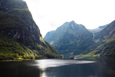 Norveç fiyortlarında yelken açan bir gemi. Fiyort ve dağlarla inanılmaz doğa manzarası. Güzel bir yansıma. Seyahat, yaşam tarzı, macera, vahşi doğa konsepti.
