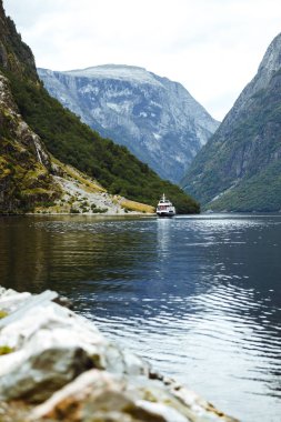 Norveç fiyortlarında yelken açan bir gemi. Fiyort ve dağlarla inanılmaz doğa manzarası. Güzel bir yansıma. Seyahat, yaşam tarzı, macera, vahşi doğa konsepti.