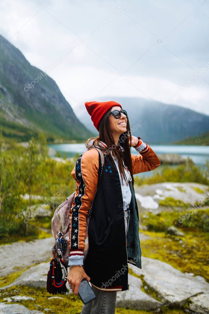 Stylish young woman enjoys freedom against the backdrop of the mountains in the Norway. The girl tourist enjoys the beautiful scenery  majestic mountains. Travelling, lifestyle, adventure, concept.