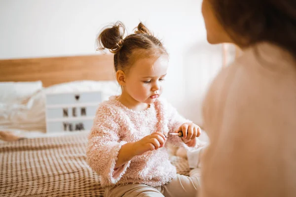 Little girl doing makeup to mom. Mother and daughter have fun together. The daughter paints lips to my mother. Happy loving family.