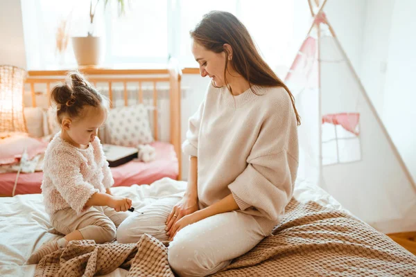 Little girl doing makeup to mom. Mother and daughter have fun together. The daughter paints lips to my mother. Happy loving family.