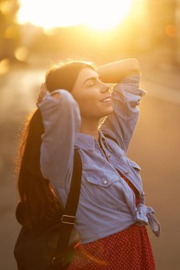  Gün batımında güzel genç bir kadının portresi. Genç kız şehir caddesinde gün ışığının tadını çıkarıyor. İnsanlar, yaşam tarzı, seyahat ve tatil kavramı.                                 
