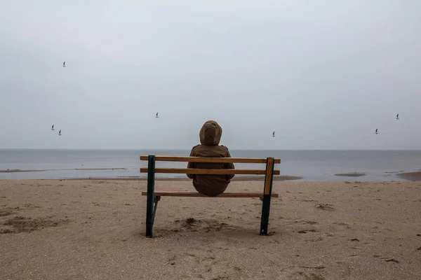 Loneliness human sitting on a bench at the seashore. Foggy morning at sea.