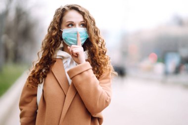 Yüzünde steril tıbbi maske takan kız bir jest gösteriyor: Sessizlik. Salgının yayılmasını önleme ve koronavirüsü tedavi etme kavramı karantina şehrinde salgındır.. 