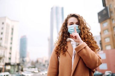 Yüzünde steril tıbbi maske takan kız bir jest gösteriyor: Sessizlik. Salgının yayılmasını önleme ve koronavirüsü tedavi etme kavramı karantina şehrinde salgındır.. 