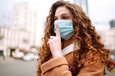 Yüzünde steril tıbbi maske takan kız bir jest gösteriyor: Sessizlik. Salgının yayılmasını önleme ve koronavirüsü tedavi etme kavramı karantina şehrinde salgındır.. 