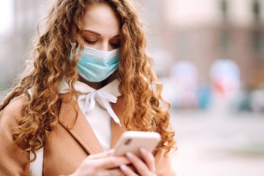Yüzünde karantina şehrinde bir telefonla steril tıbbi maske takan bir kız. Haber aramak için telefonu kullanan bir kadın. Salgının yayılmasını önleme konsepti.