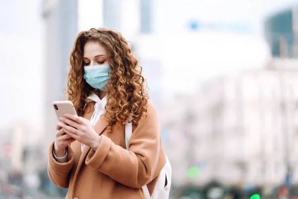도시에서 의료용 마스크를 소녀가 핸드폰을 있습니다 뉴스를 전화를 사용하는 전염병의 — 스톡 사진