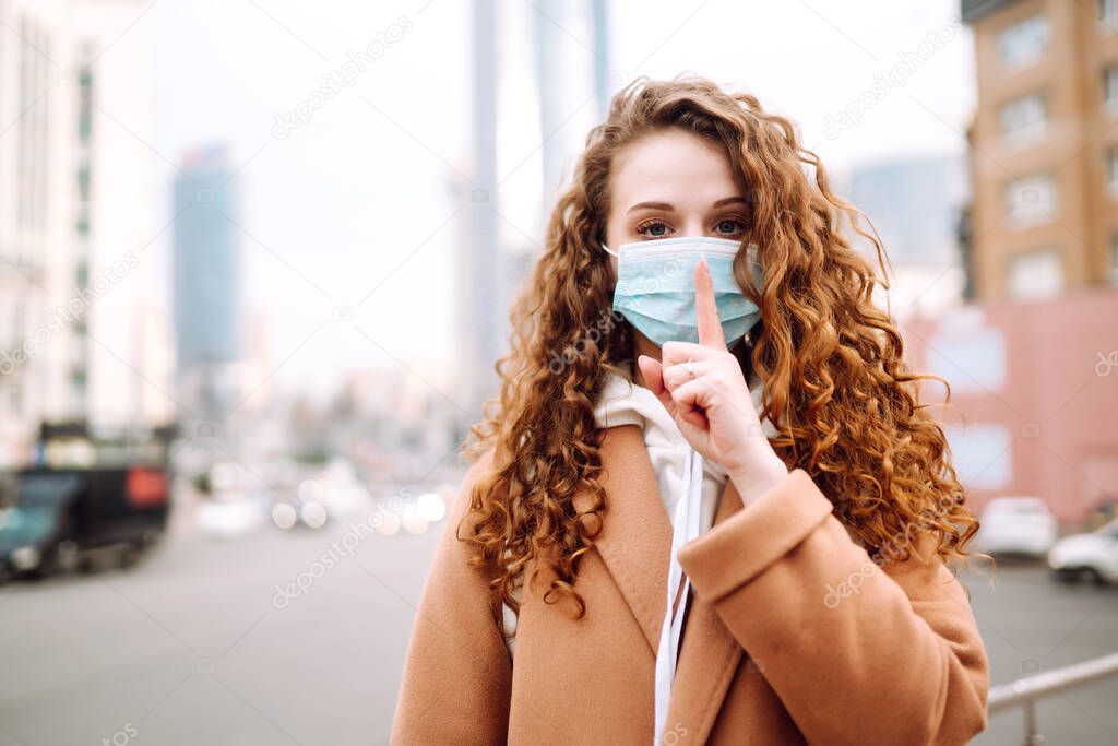 Girl in protective sterile medical mask on her face shows a gesture: shh. silence. The concept of preventing the spread of the epidemic and treating coronavirus, pandemic in quarantine city. 