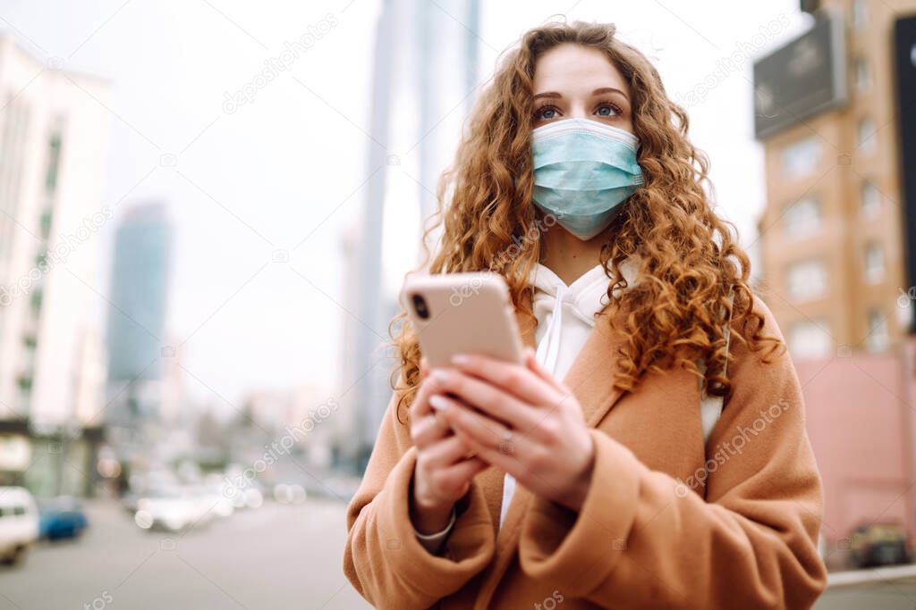 Girl in protective sterile medical mask on her face with a phone in  quarantine city. Woman using the phone to search for news. The concept of preventing the spread of the epidemic.