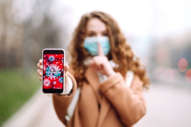 Yüzünde steril tıbbi maske takan kız telefonu karantina şehrinde tutuyor. Coronavirus hücreleri telefon ekranında. Salgının yayılmasını önleme konsepti. 