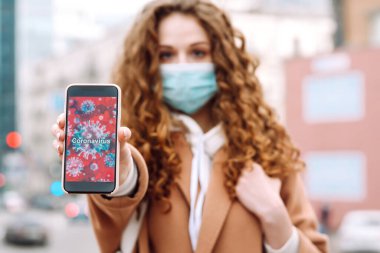 Yüzünde steril tıbbi maske takan kız telefonu karantina şehrinde tutuyor. Coronavirus hücreleri telefon ekranında. Salgının yayılmasını önleme konsepti. 