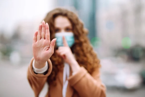 Hand stop sign. Woman in a sterile medical mask on her face, shows stop hands gesture for stop coronavirus outbreak. The concept of preventing the spread of the epidemic.