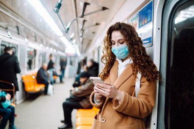 Korunaklı steril tıbbi maskeli bir kız metroda telefonuyla yüzünde. Coronavirus hakkında haber aramak için telefonu kullanan bir kadın. Salgının yayılmasını önleme konsepti.