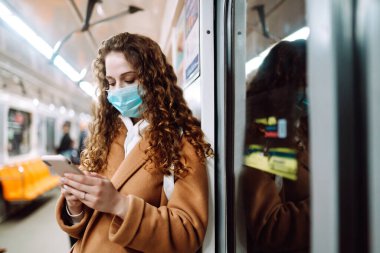 Korunaklı steril tıbbi maskeli bir kız metroda telefonuyla yüzünde. Coronavirus hakkında haber aramak için telefonu kullanan bir kadın. Salgının yayılmasını önleme konsepti.