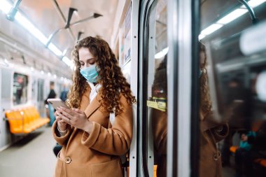 Korunaklı steril tıbbi maskeli bir kız metroda telefonuyla yüzünde. Coronavirus hakkında haber aramak için telefonu kullanan bir kadın. Salgının yayılmasını önleme konsepti.