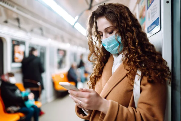 Korunaklı steril tıbbi maskeli bir kız metroda telefonuyla yüzünde. Coronavirus hakkında haber aramak için telefonu kullanan bir kadın. Salgının yayılmasını önleme konsepti.