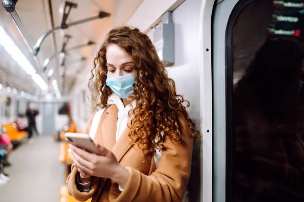 Korunaklı steril tıbbi maskeli bir kız metroda telefonuyla yüzünde. Coronavirus hakkında haber aramak için telefonu kullanan bir kadın. Salgının yayılmasını önleme konsepti.
