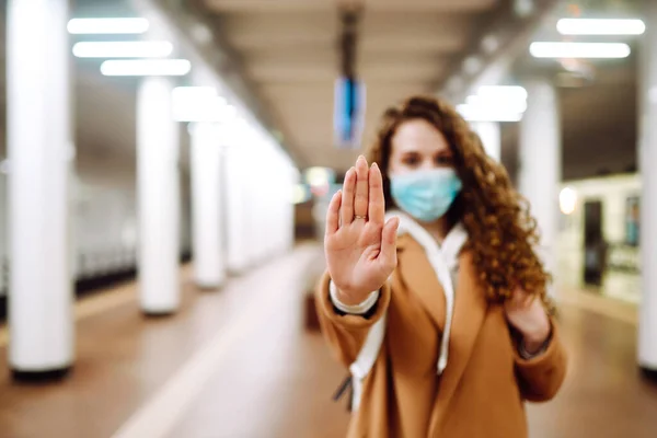 Hand stop sign. Woman in a sterile medical mask on her face, shows stop hands gesture for stop coronavirus outbreak at subway station. The concept of preventing the spread of the epidemic.