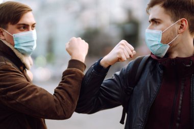 Yüzünde koruyucu tıbbi maske takan arkadaşları dirseklerini karantina şehrinde selamlıyorlar. Dirsek çarpması, koronavirüsün yayılmasını önlemek için yeni bir selamlamadır. El sıkışmayın. El sıkışmayı kesin..