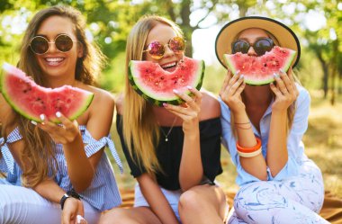 Üç güzel genç kız birlikte eğleniyor ve sıcak yaz gününde karpuz yiyorlar. Arkadaşları bir dilim karpuz tutuyor ve parkta poz veriyorlar. Yaz konsepti.