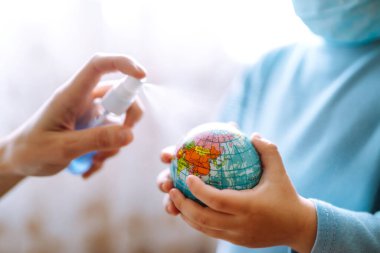 Dünya küresi tutan steril tıbbi maskeli bir çocuk. Gezegeni kurtar. Gezegen sterilizasyonu. Salgın koronavirüsün yayılmasını önleme konsepti.