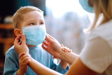 Tıbbi maskeli küçük bir çocuk ve anne. Anne, bebek steril tıbbi maskesini takıyor. Çocuk, yüz maskesi takıyor, karantinada virüs, salgın ve salgın hastalıklardan korunuyor..