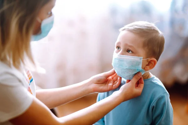 Little boy and mom in medical mask. Mother puts on her baby sterile medical mask. Child, wearing face mask, protect from infection of virus, pandemic, outbreak and epidemic of disease on quarantine.
