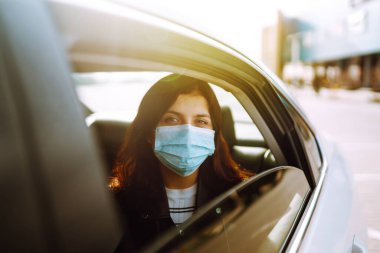 Yüzünde steril tıbbi maske takan bir kız takside oturuyor. Salgının yayılmasını önleme ve koronavirüsü tedavi etme kavramı, karantina şehrinde salgın. Sağlık hizmetleri kavramı