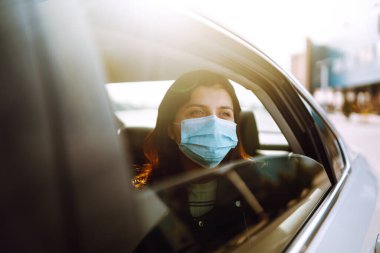 Girl in protective sterile medical mask on her face is sitting in a taxi. The concept of preventing the spread of the epidemic and treating coronavirus, pandemic in quarantine city. Healthcare concept clipart