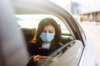 Yüzünde steril tıbbi maske olan kız takside telefonla konuşuyor. Salgının yayılmasını önleme ve koronavirüsü tedavi etme kavramı karantina şehrinde salgındır..