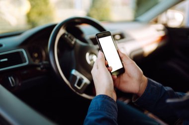El telefonu arabanın direksiyonunun arka planına doğru tutar. Yazı veya resim için boş ekranlı bir telefon. Ulaşım ve araç kavramı. 