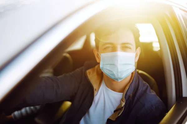 Koruyucu steril tıbbi maskeli genç adam araba kullanıyor. Salgının yayılmasını önleme ve koronavirüsü tedavi etme kavramı, karantina şehrinde salgın. Covid - 19.