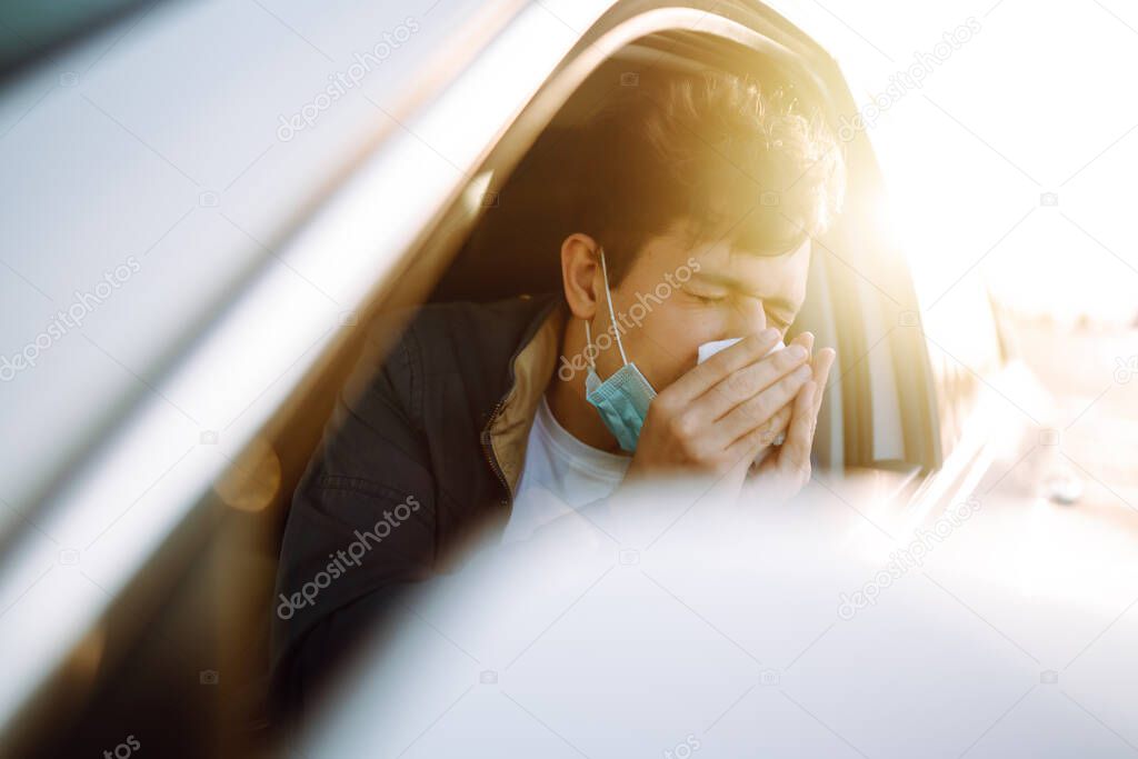 Young man coughing and sneezing into a handkerchief while driving a car. The concept of preventing the spread of the epidemic and treating coronavirus, pandemic in quarantine city. Covid -19.