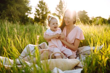 Anne ve küçük kızı gün batımında bir yaz parkında birlikte oynuyorlar. Küçük çocuklu mutlu bir anne güneşli bir alanda eğleniyor. Öpücükler ve sarılmalar. Mutlu aile kavramı.. 