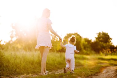Anne ve küçük kızı gün batımında bir yaz parkında birlikte oynuyorlar. Küçük çocuklu mutlu bir anne güneşli bir alanda eğleniyor. Öpücükler ve sarılmalar. Mutlu aile kavramı.. 