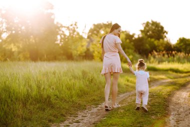 Anne ve küçük kızı gün batımında bir yaz parkında birlikte oynuyorlar. Küçük çocuklu mutlu bir anne güneşli bir alanda eğleniyor. Öpücükler ve sarılmalar. Mutlu aile kavramı.. 