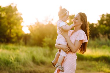 Anne ve küçük kızı gün batımında bir yaz parkında birlikte oynuyorlar. Küçük çocuklu mutlu bir anne güneşli bir alanda eğleniyor. Öpücükler ve sarılmalar. Mutlu aile kavramı.. 